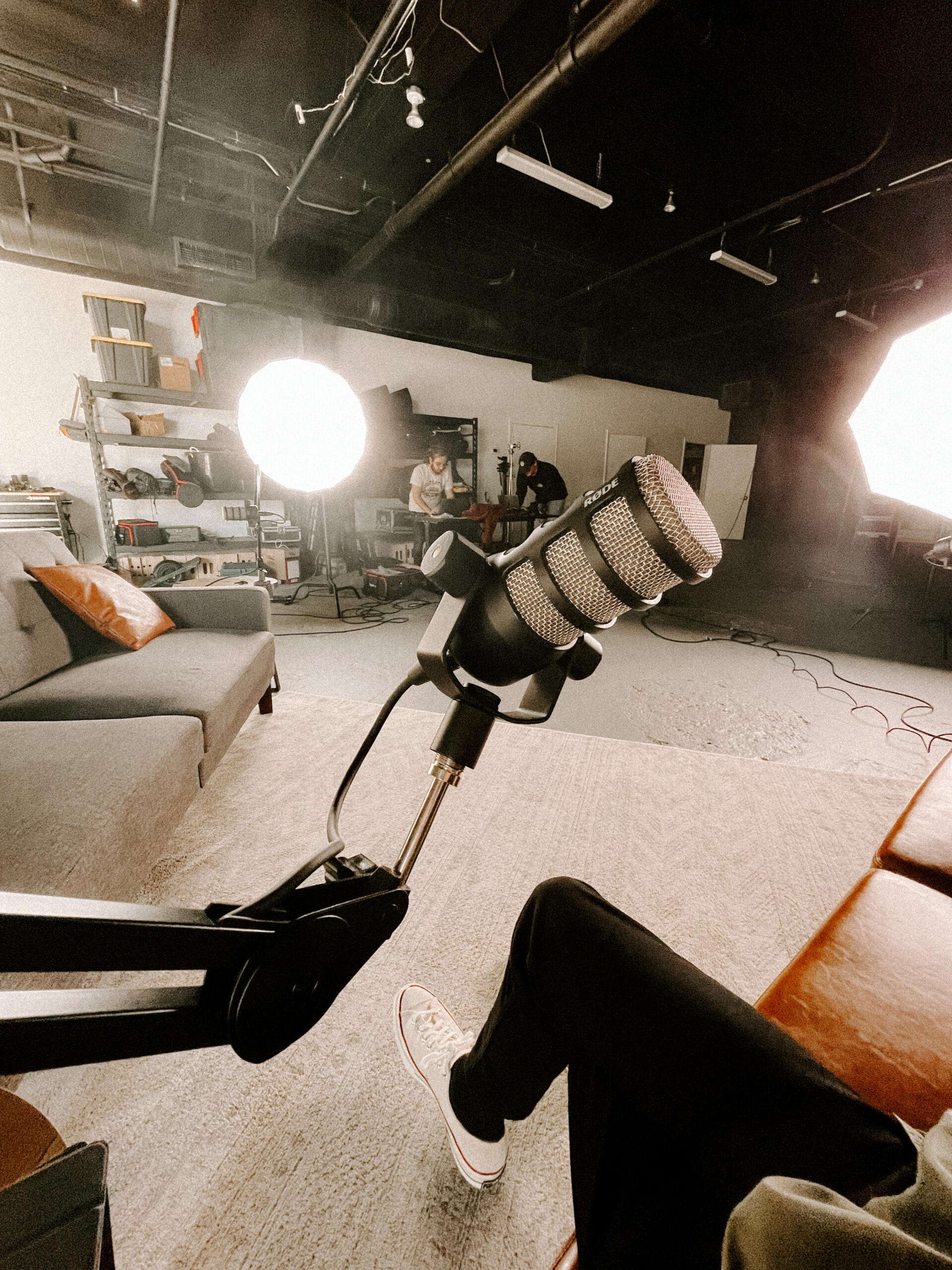 Image of a podcast studio, microphone in the foreground and people working in the background.